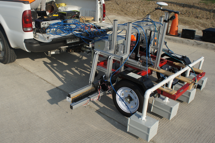 A truck with a row of four scanning devices spaced out behind. Each is about the size of a cinder block.